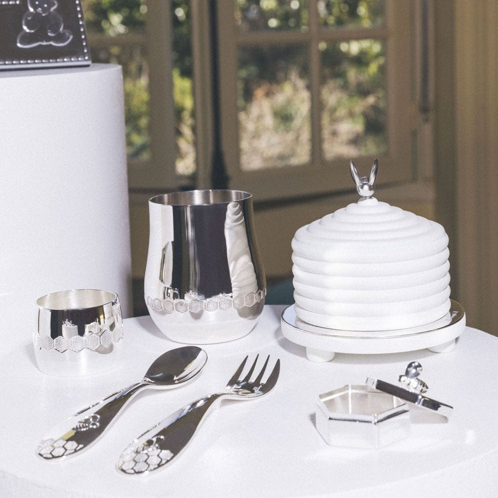 Christofle Beebee silver-plated baby spoon with a raised bumblebee motif on the handle set on the table with a Beebee fork, box, music box, cup and napkin ring.