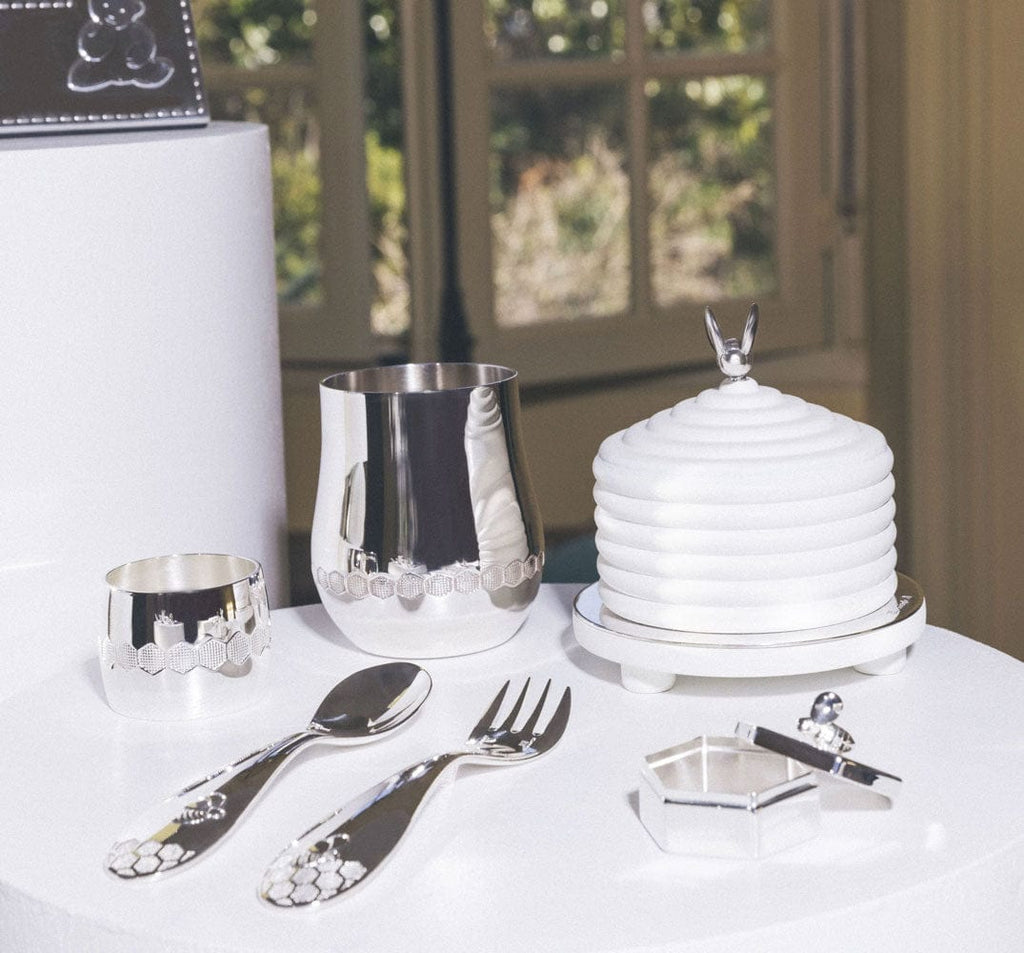 Christofle Beebee silver-plated baby spoon with a raised bumblebee motif on the handle set on the table with a Beebee fork, box, music box, cup and napkin ring.